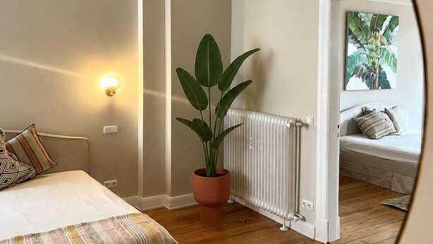 A bedroom with a bed, a potted plant, a radiator, and a painting on the wall. - Luxury old building within walking distance of the city center - Lübeck's best location - water view (Lübeck)