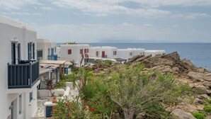 A coastal village with white buildings, rocky terrain, and a view of the sea. - Traditional Mykonian Studio – Beachfront, Pool, Garden, Sea Views (Mykonos)