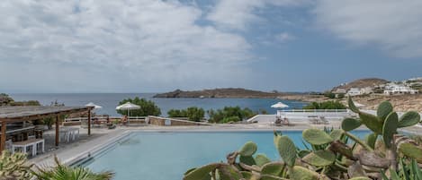 A pool area with a view of the sea, surrounded by cacti and a wooden pergola.