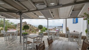 An outdoor patio with stone flooring, white furniture, and a view of the sea. - Traditional Mykonian Studio – Beachfront, Pool, Garden, Sea Views (Mykonos)
