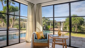 A room with large windows, a pool, a chair, and a table.