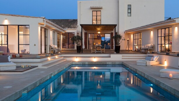 A modern house with a swimming pool, outdoor seating, and a well-lit entrance.
