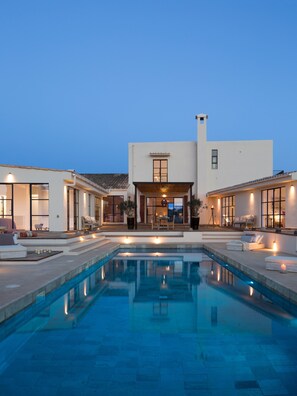 Ein modernes Haus mit Schwimmbad, Sitzgelegenheiten im Freien und einem gut beleuchteten Eingangsbereich.