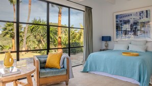 A bedroom with a large window, a bed, a sofa, and a table.
