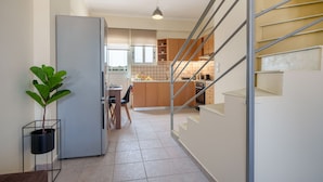 A modern kitchen with a refrigerator, a dining area, and a staircase leading to another level. - Apartment 'Solomos' with Sea View, Wi-Fi and Air Conditioning (Elios Proni)