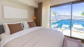 A hotel room with a large bed, a view of boats and a marina, and a large window.