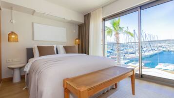 Ein Schlafzimmer mit einem großen Bett, einem Nachttisch, einer Bank und Blick auf eine Marina mit Booten, sowie einem großen Fenster.