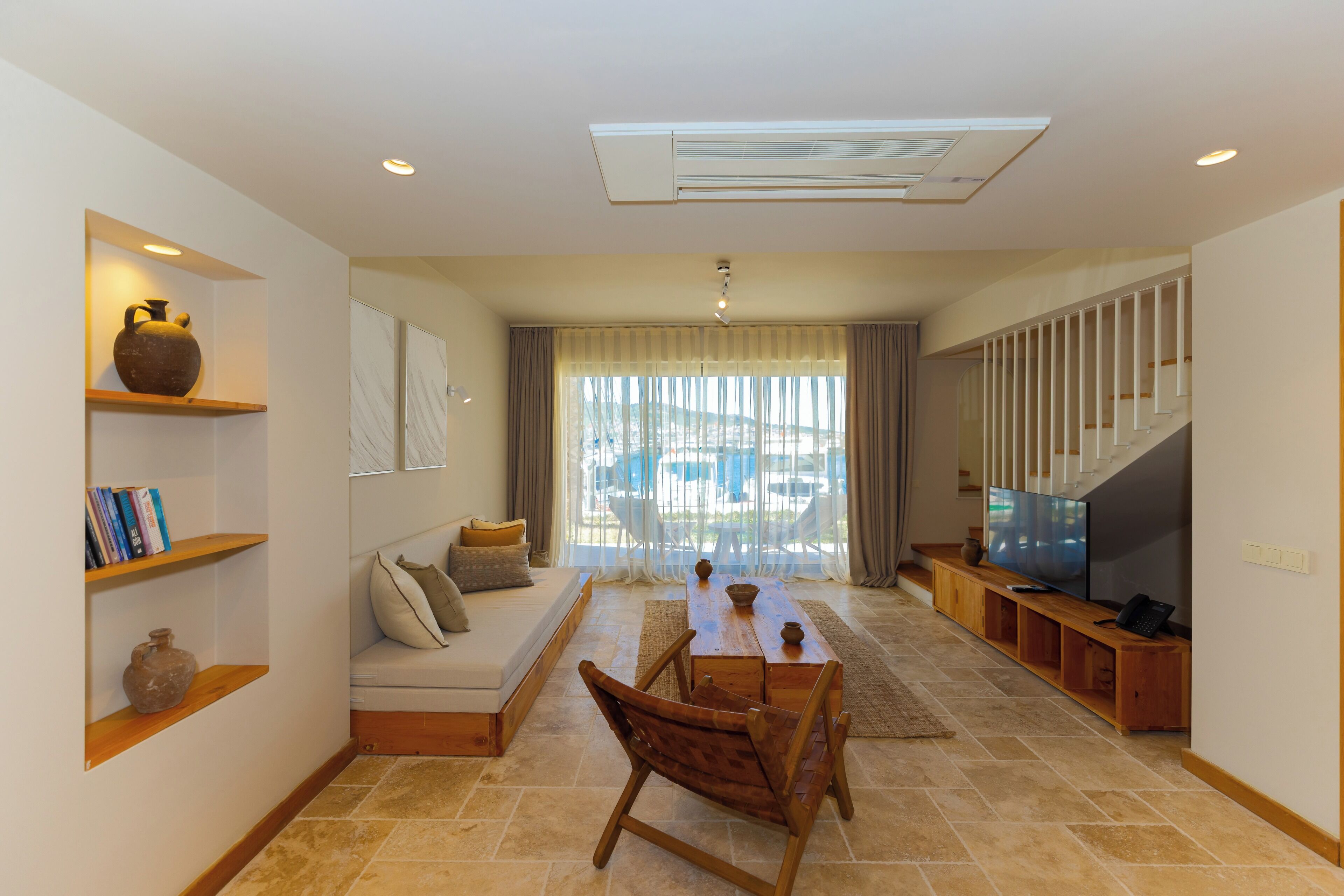 Un salón con sofá, mesa de centro de madera, televisor y estanterías con libros y jarrones.