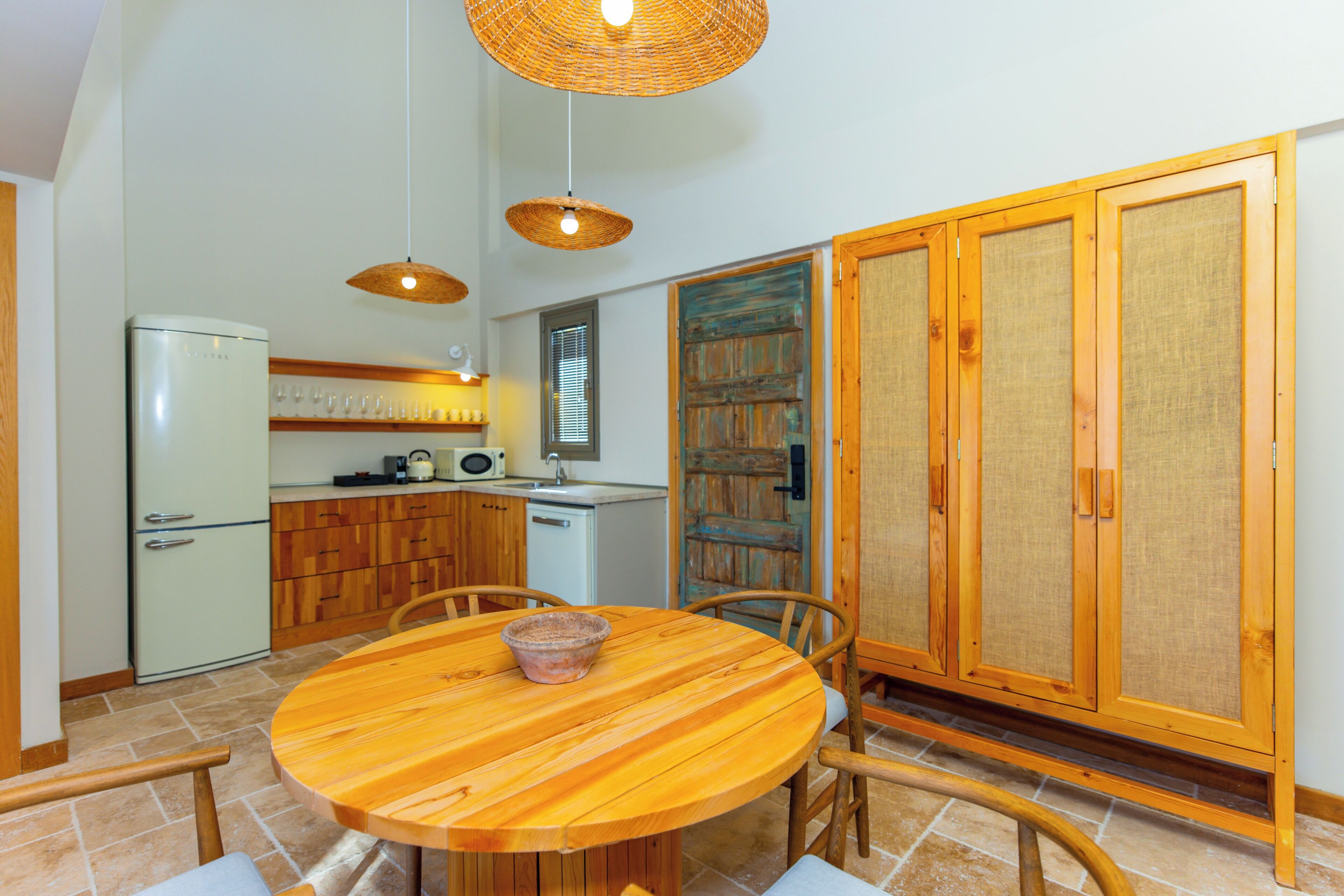 A kitchen with a round wooden table, chairs, a refrigerator, and wooden cabinets.