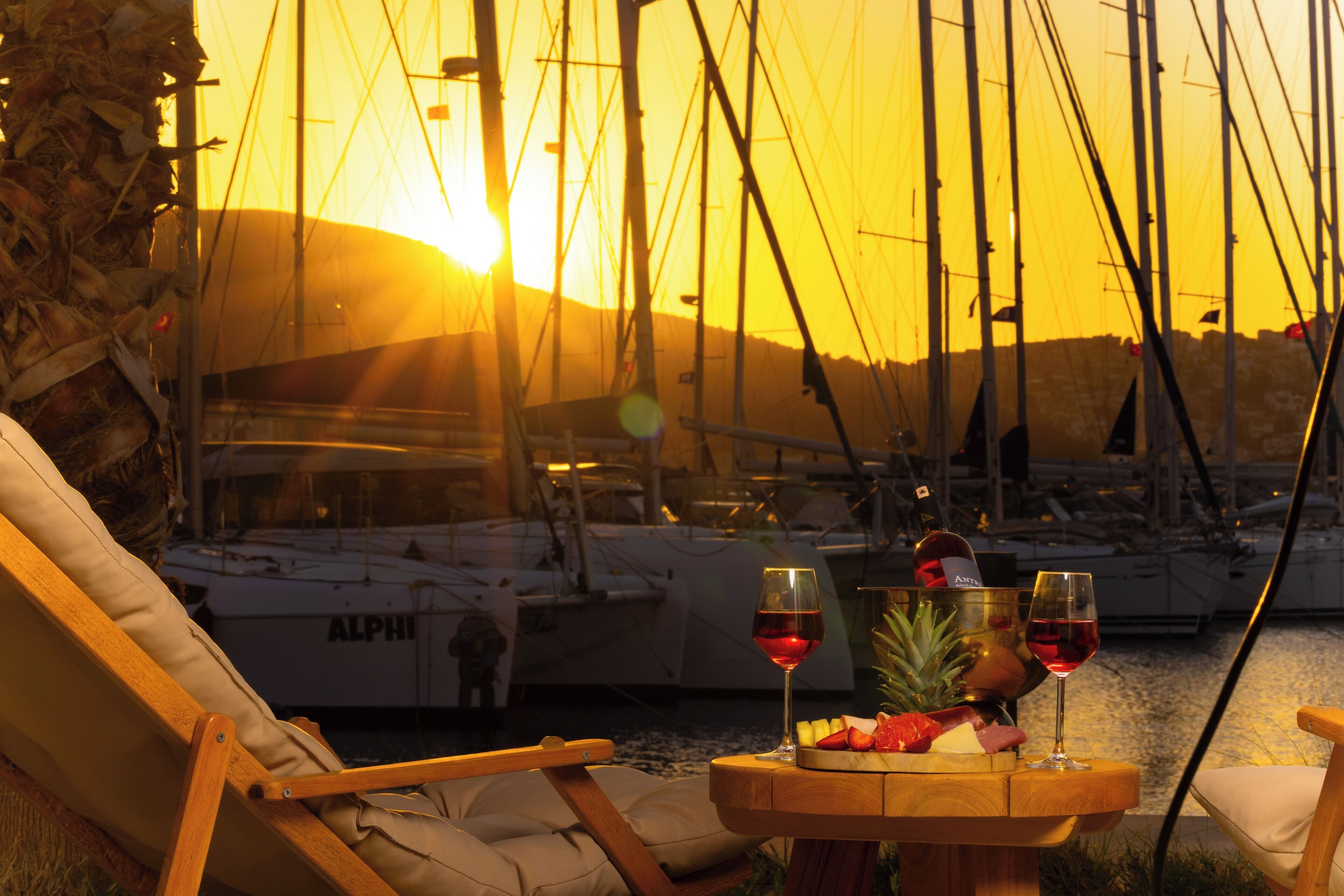 A wooden table with a bottle of wine, two glasses, and a fruit platter.
