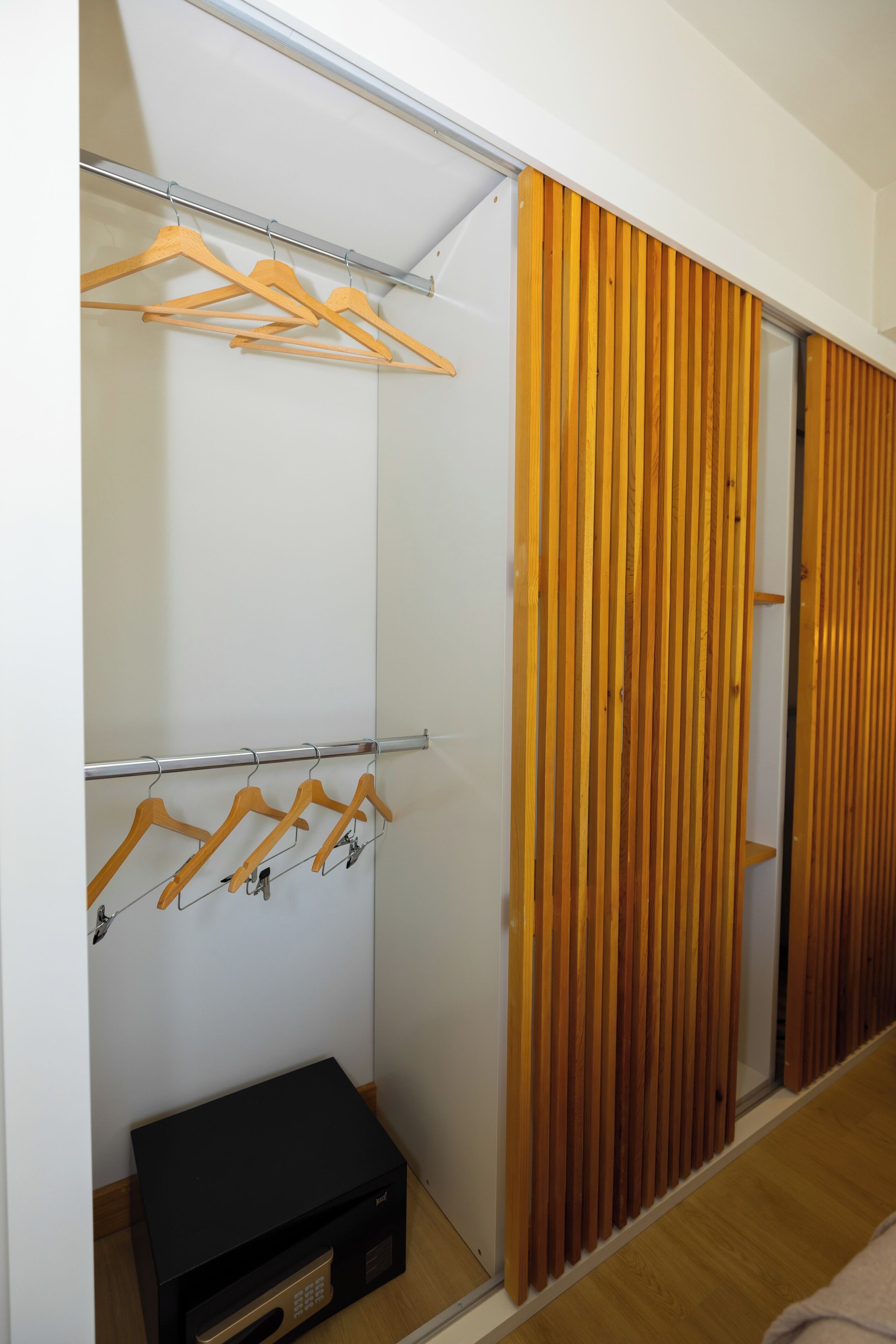 Ein moderner Kleiderschrank mit Holzaufhängern, einer schwarzen Aufbewahrungsbox und einer Schiebetür mit vertikalen Holzleisten.