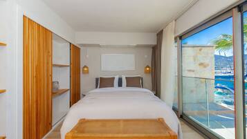 Une chambre moderne avec un grand lit, une armoire en bois et une vue sur une marina, visible à travers une porte vitrée.