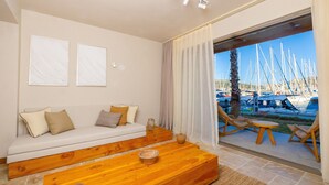 A modern living room with a sofa, wooden coffee table, and a view of a marina through a glass door.