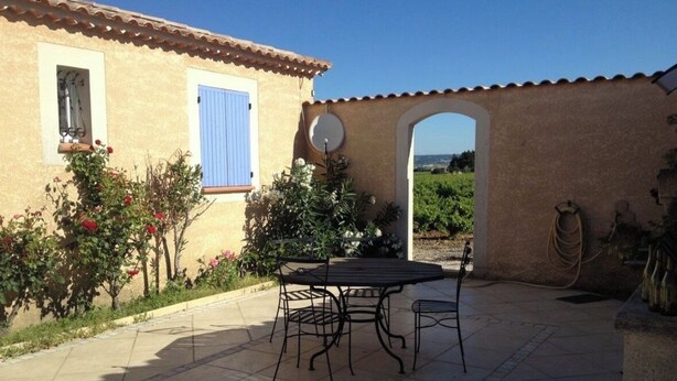 Une terrasse avec une table et des chaises, une fenêtre bleue et une vue à travers une arche.