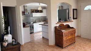 Une cuisine avec des meubles blancs, une commode en bois et un sol carrelé.