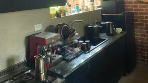 Une cuisine équipée d’une cuisinière, d’un évier et de divers appareils électroménagers. Il y a une fenêtre au-dessus de l’évier et un mur de briques derrière.