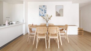 Eine moderne Küche mit Essbereich, ausgestattet mit einer weißen Arbeitsplatte, Holzstühlen und zwei Wandbildern.