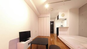 Um espaço de estar moderno e compacto, com televisão de tela plana, mesa pequena, sofá e cama.