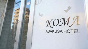 Placa de hotel com o nome 'KOMA ASAKUSA HOTEL' e vista parcial da fachada de um edifício.