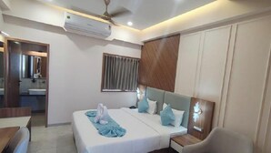 A hotel room with a bed, bedside table, and a window with blinds. - Hotel The Grand Bhagwati (Dwarka)