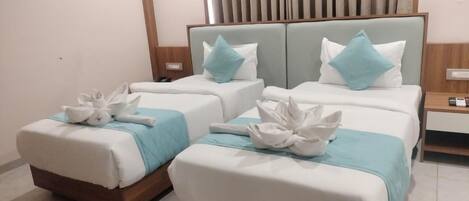 Habitación de hotel con tres camas, cada una con una colcha blanco y azul, y cabeceros de madera.