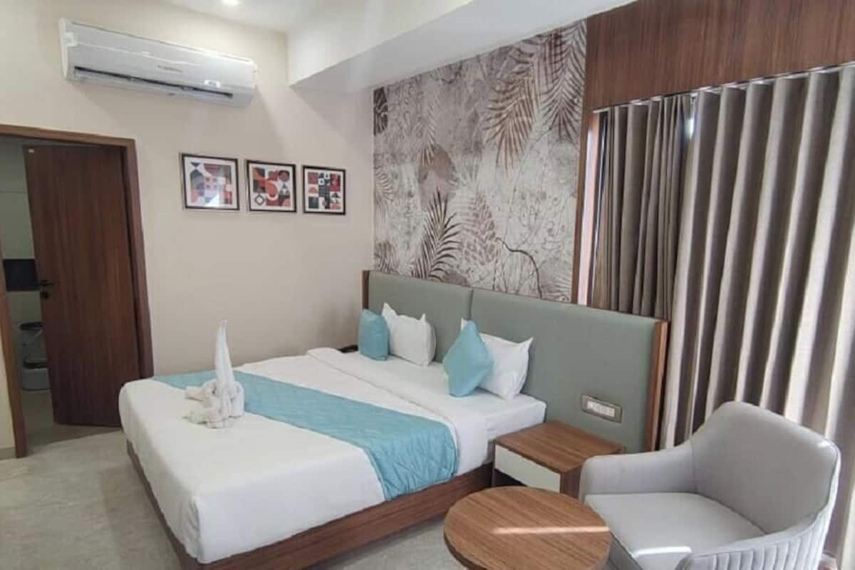 Habitación de hotel con cama, una silla, mesita de noche, aire acondicionado y cortina.