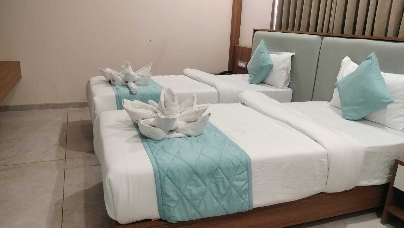 A hotel room with two beds, each with a white bedspread and a teal quilted blanket.