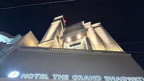 A hotel entrance with steps leading up to a glass door, a sign above the door, and a person standing in front. - Hotel The Grand Bhagwati (Dwarka)