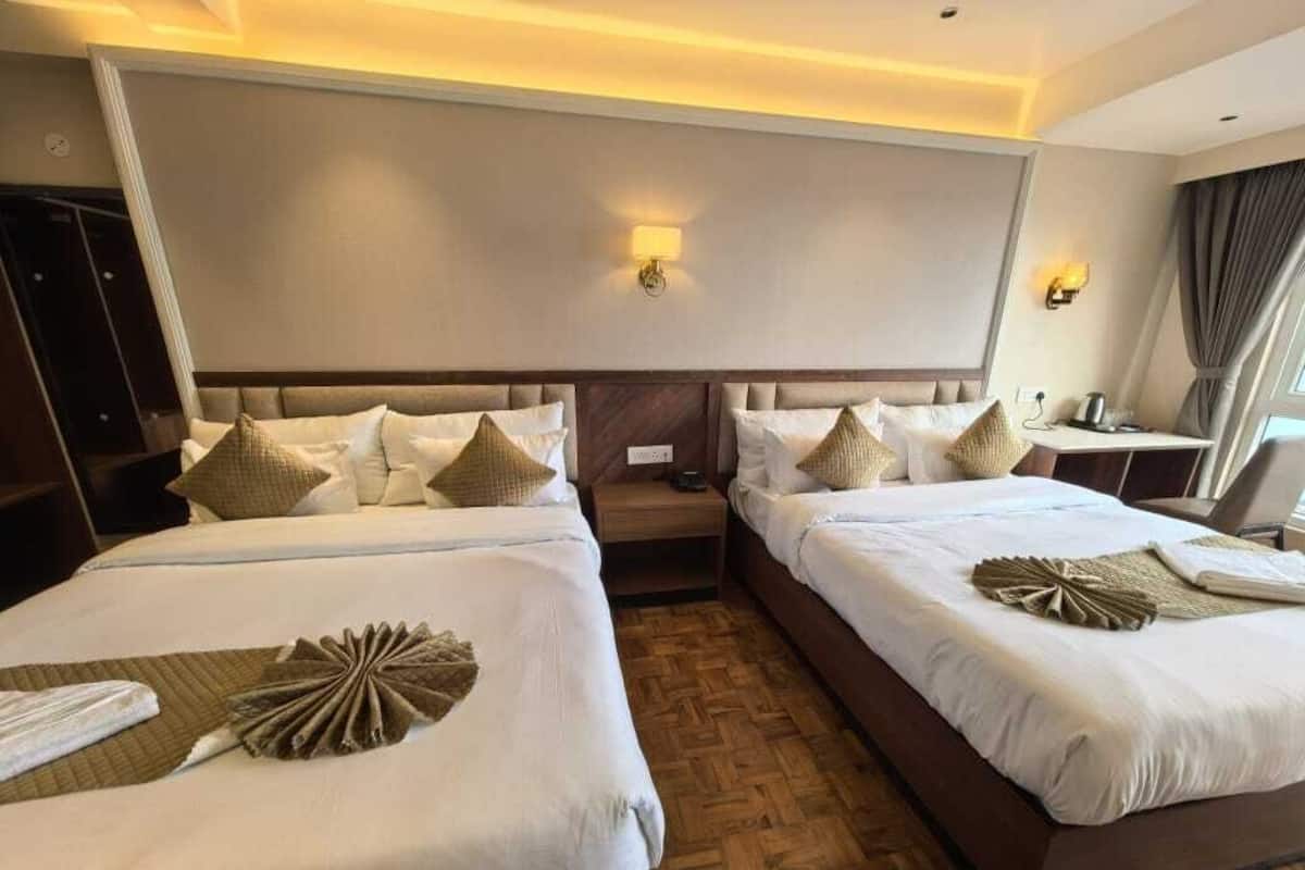 A hotel room with two beds, a wooden floor, and a large window with curtains.