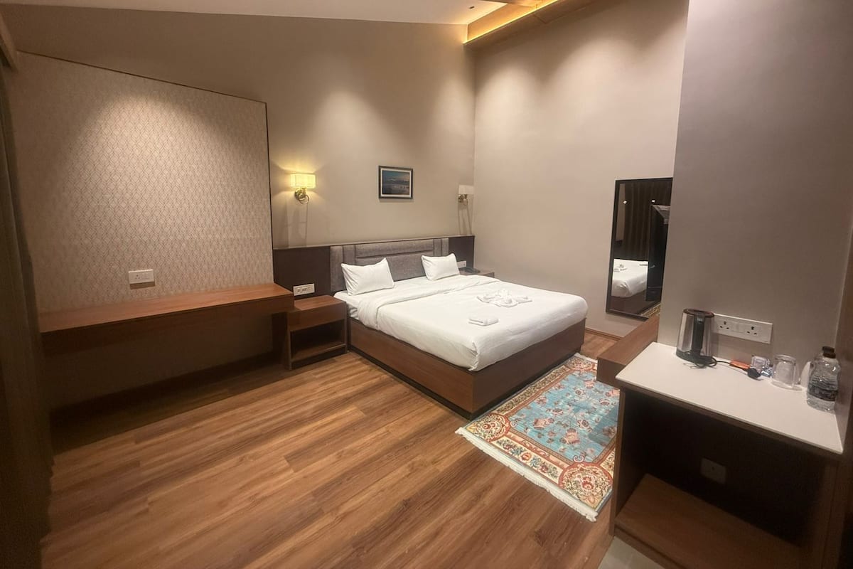 A modern hotel room with a large bed, bedside tables, a mirror, and a small desk area.