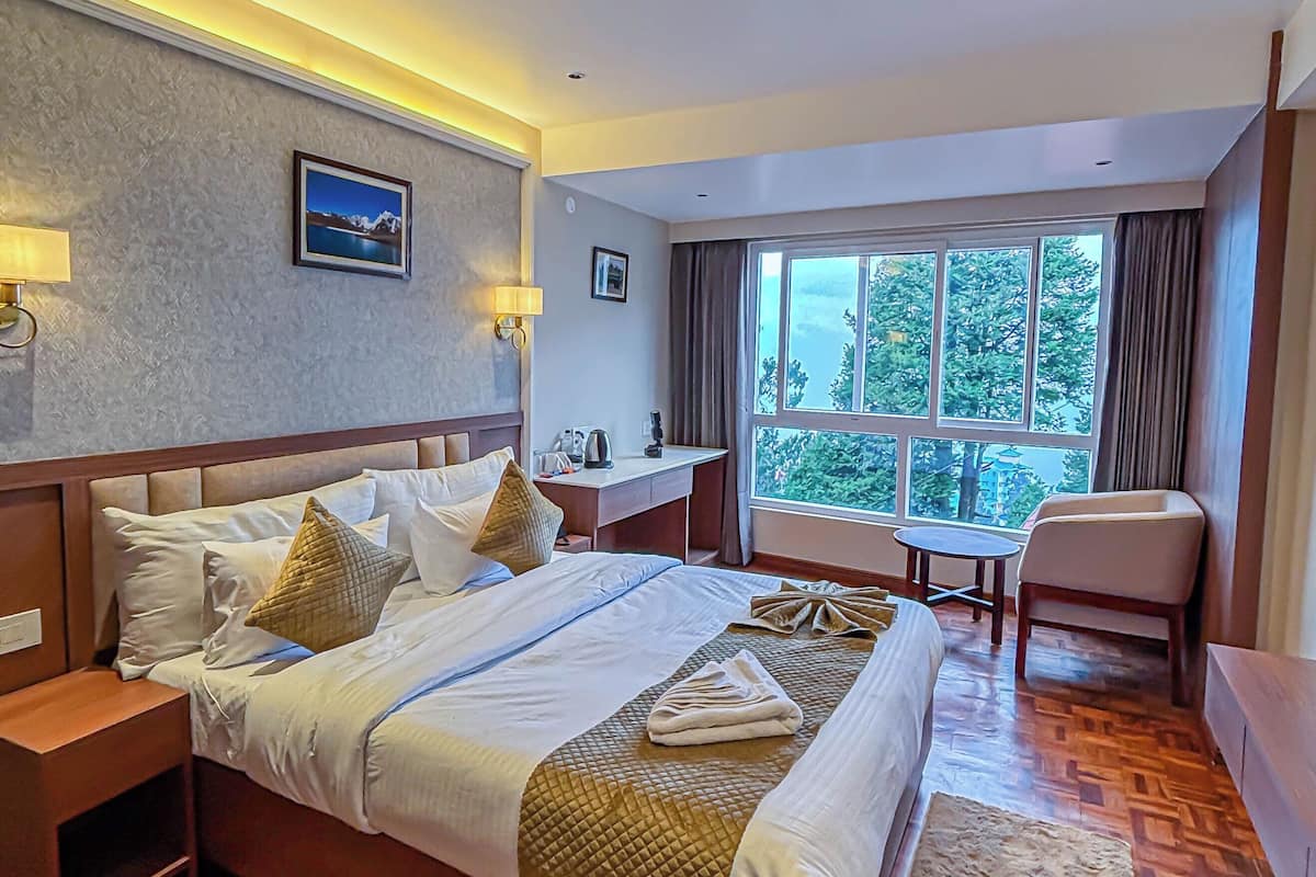 A hotel room with a large bed, bedside tables, a desk, a chair, and a large window.