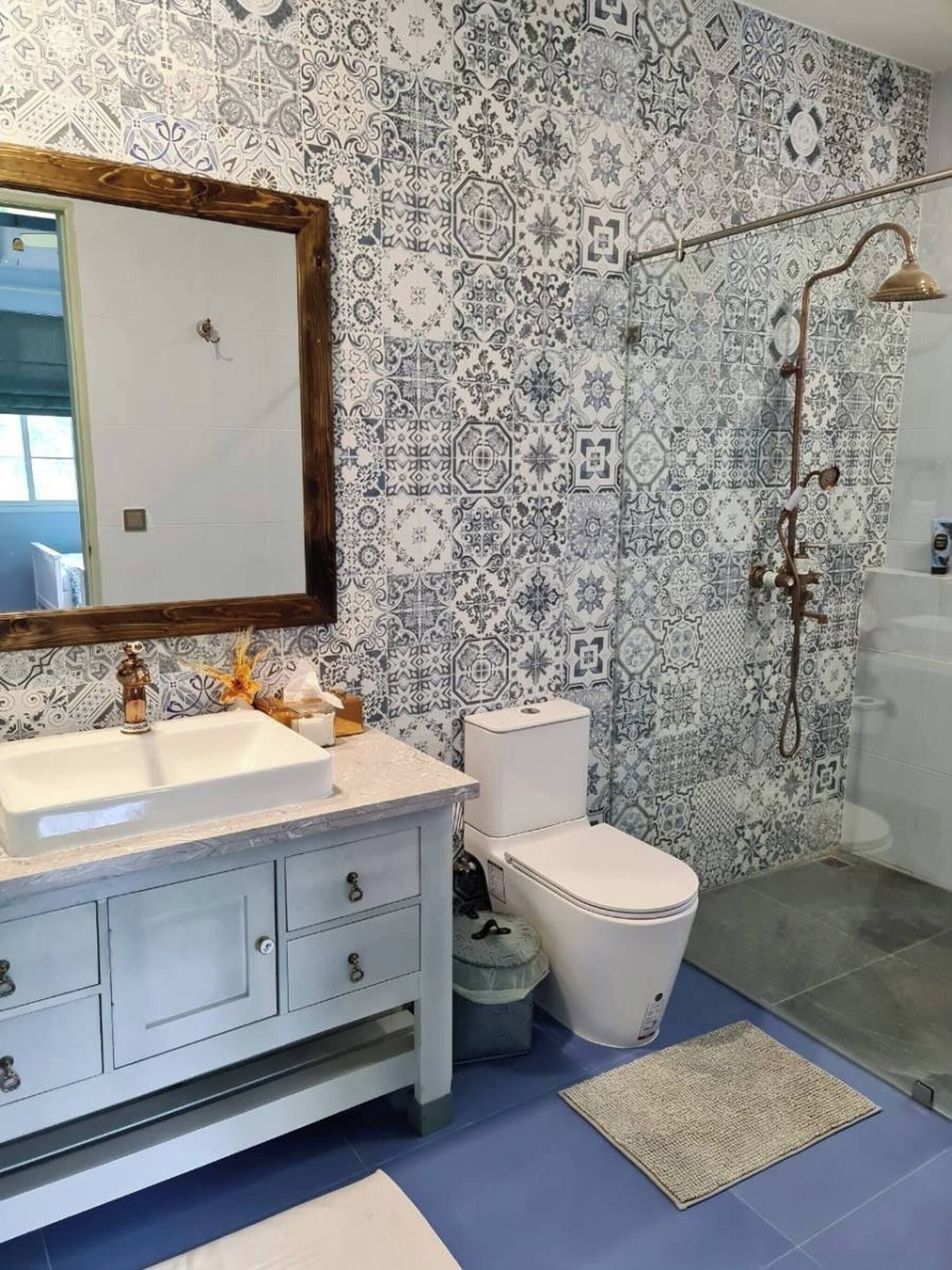 A bathroom with a patterned tile wall, a white sink, a toilet, and a shower with a handheld showerhead.