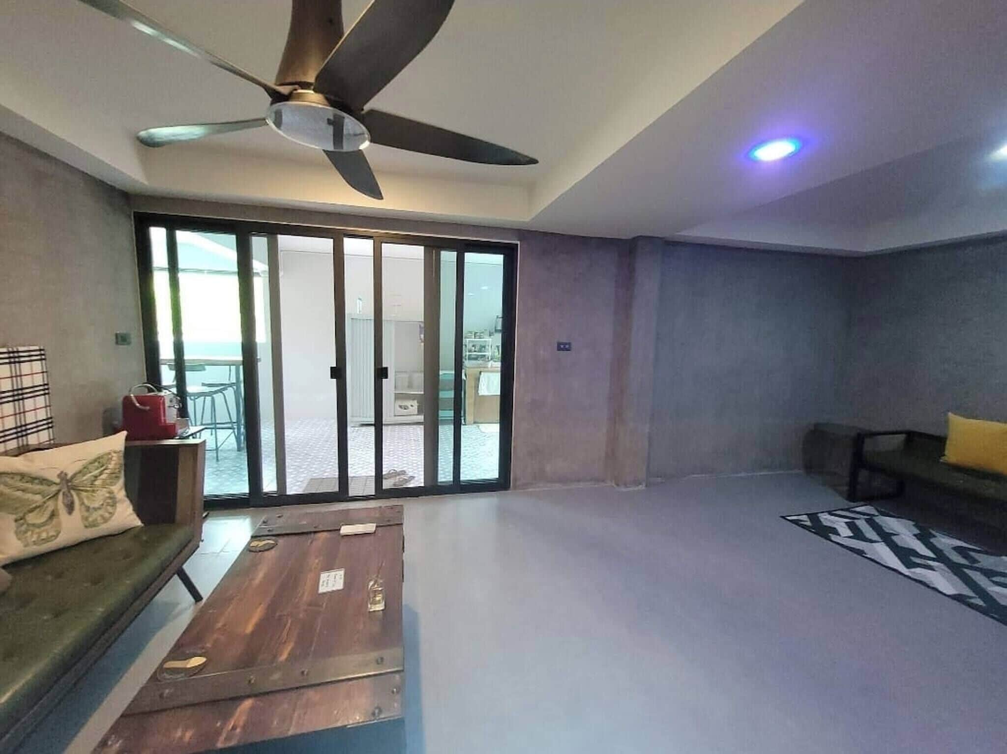 A spacious living area with a ceiling fan, a sliding glass door leading to an outdoor balcony, a sofa, and a coffee table.