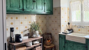 Eine Küche mit grünen Schränken, einer Kaffeemaschine, einem Spülbecken und einem Fenster mit Vorhängen.