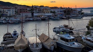 Ein Hafen mit vertäuten Booten, Gebäuden im Hintergrund und einem Sonnenuntergang.