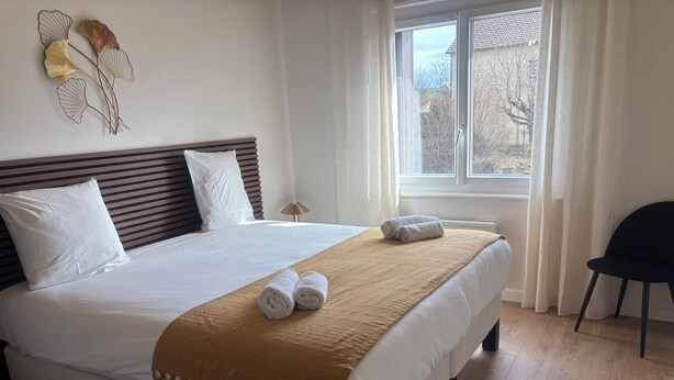 A neatly made bed with a brown throw blanket, white pillows, and two rolled towels. - Maison 3 chambres avec jardin (Langogne)