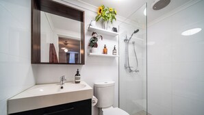 Une salle de bain moderne avec un lavabo blanc, des toilettes, une douche en verre et un miroir agrémenté d’un vase de tournesols.