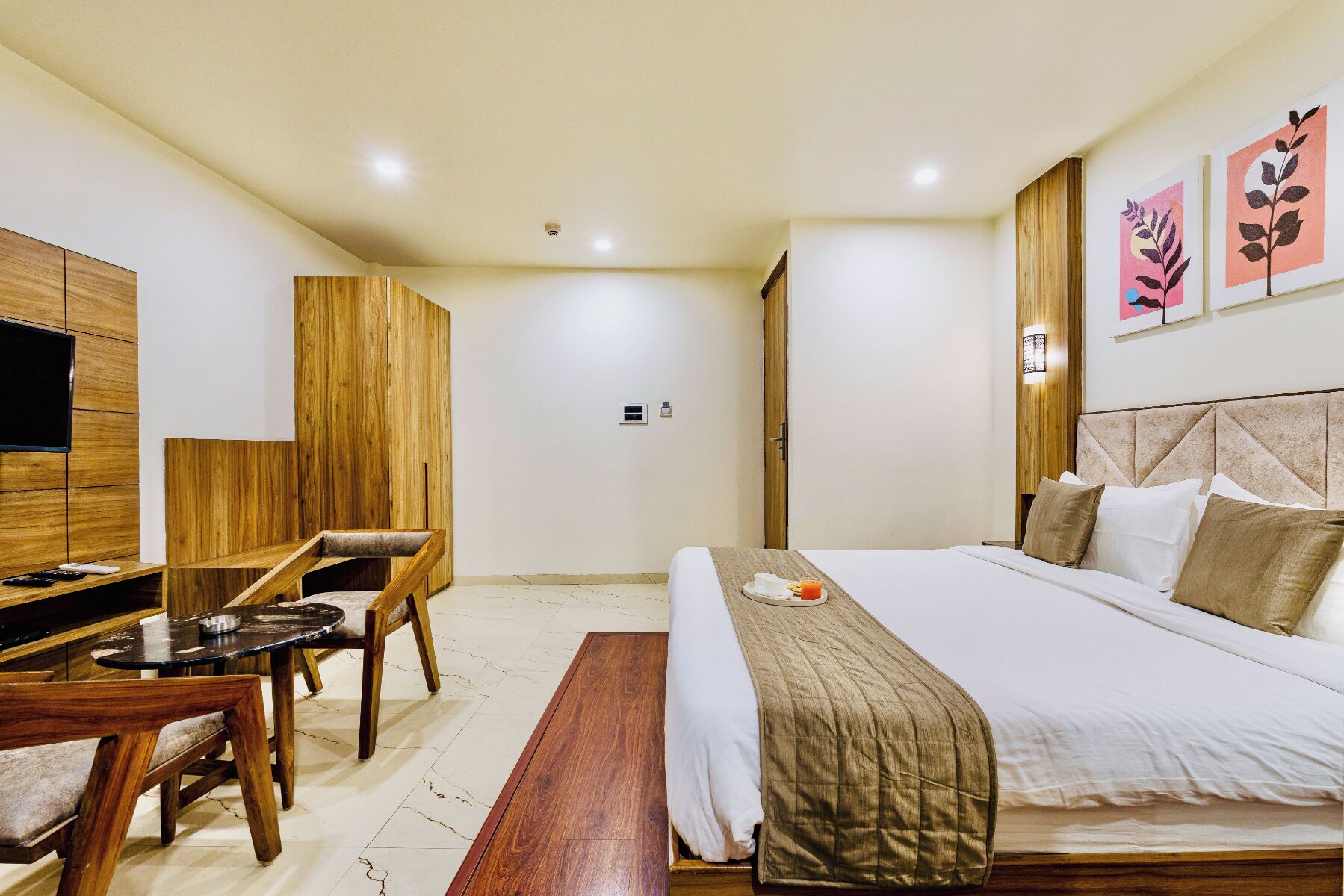 Quarto de hotel com uma cama, uma mesa com cadeira, televisão e obras de arte nas paredes.