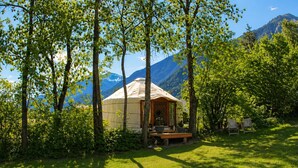 A yurt with a wooden deck and seating area, surrounded by trees and a mountainous backdrop. - WOODMOOD yurt with wellness (Leuk)
