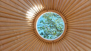 A circular skylight with wooden beams radiating outward, centered on a clear blue sky with trees. - WOODMOOD yurt with wellness (Leuk)