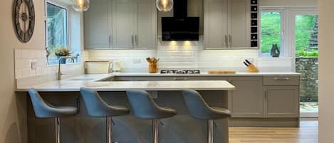 A modern kitchen with a central island, bar stools, pendant lighting, and a large window.