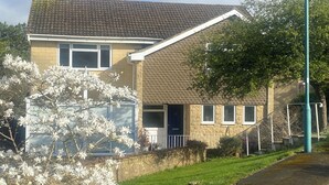 Une maison à deux étages, avec un toit en tuiles, un porche à l’avant et un petit jardin devant.