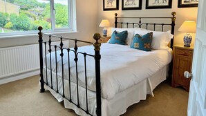 Une chambre à coucher avec un lit, une fenêtre, un radiateur, une table de chevet avec une lampe, et des tableaux encadrés accrochés au mur.