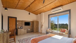 A bedroom with a bed, a desk, a TV, and a window with a view.