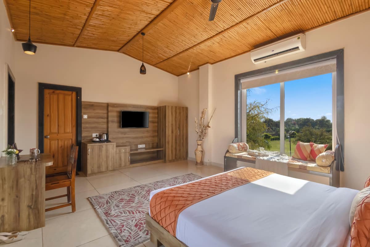 A bedroom with a bed, a desk, a TV, and a window with a view.