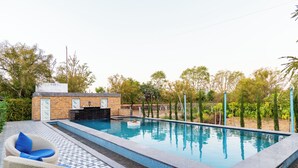 A rectangular swimming pool with a tiled edge, a lounge chair with a cushion, and a brick structure with a chimney.