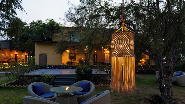 An outdoor seating area with wicker chairs and a table, surrounded by trees and a decorative hanging light fixture.