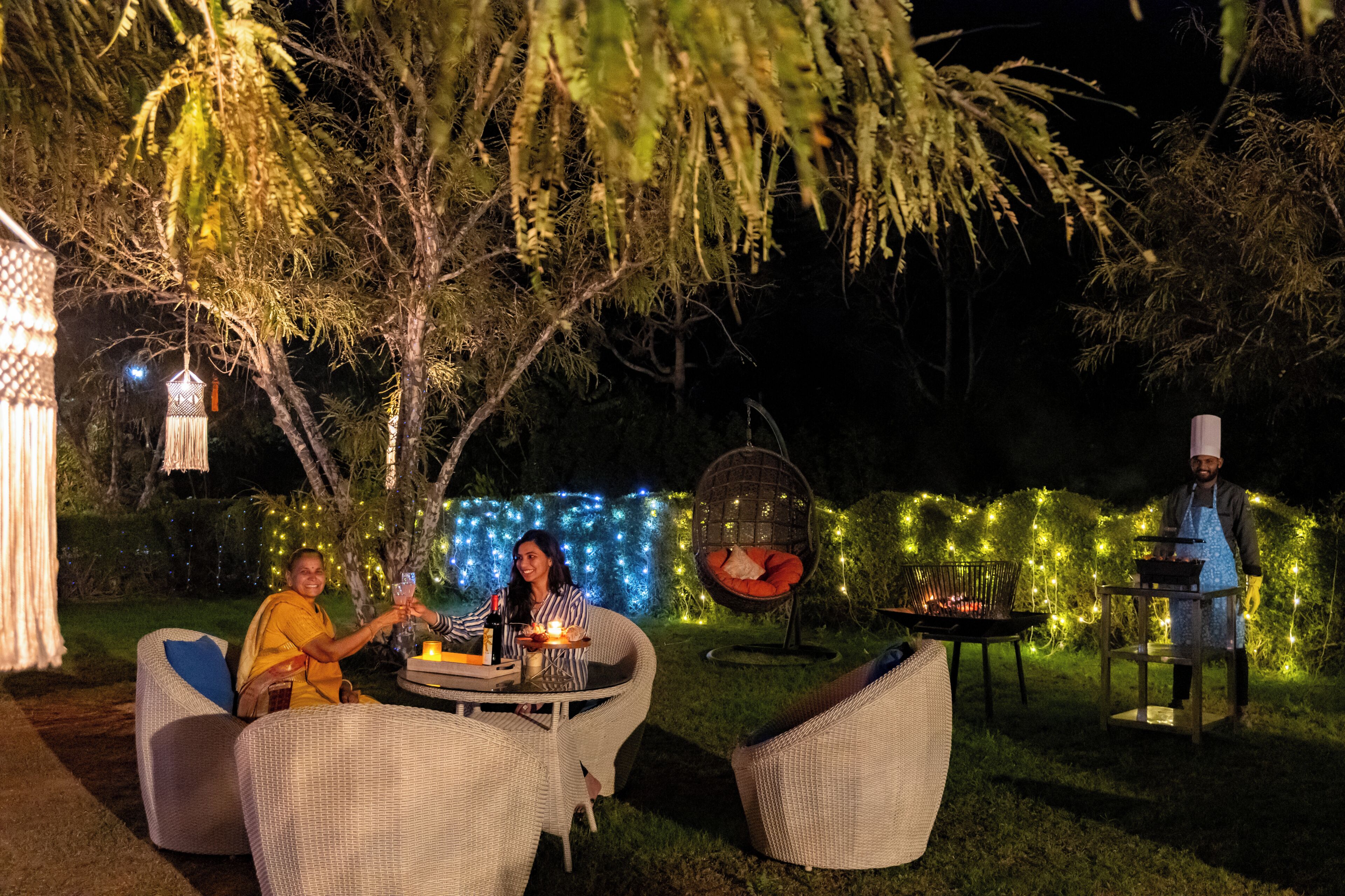Un área de comedor al aire libre con mobiliario de mimbre, una parrilla y luces colgantes.