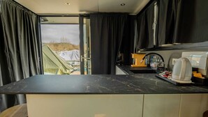 A modern kitchen with a marble countertop, a kettle, and a view of a tented area outside. - Celesia Sky water (Sesto Calende)