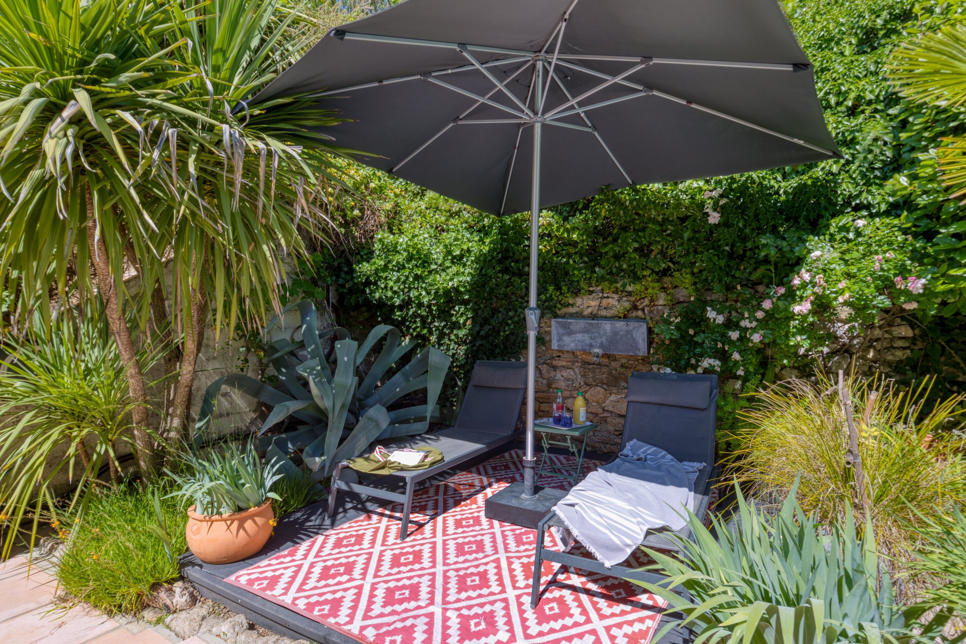 A patio with a red patterned rug, two lounge chairs, a table, and a large umbrella.
